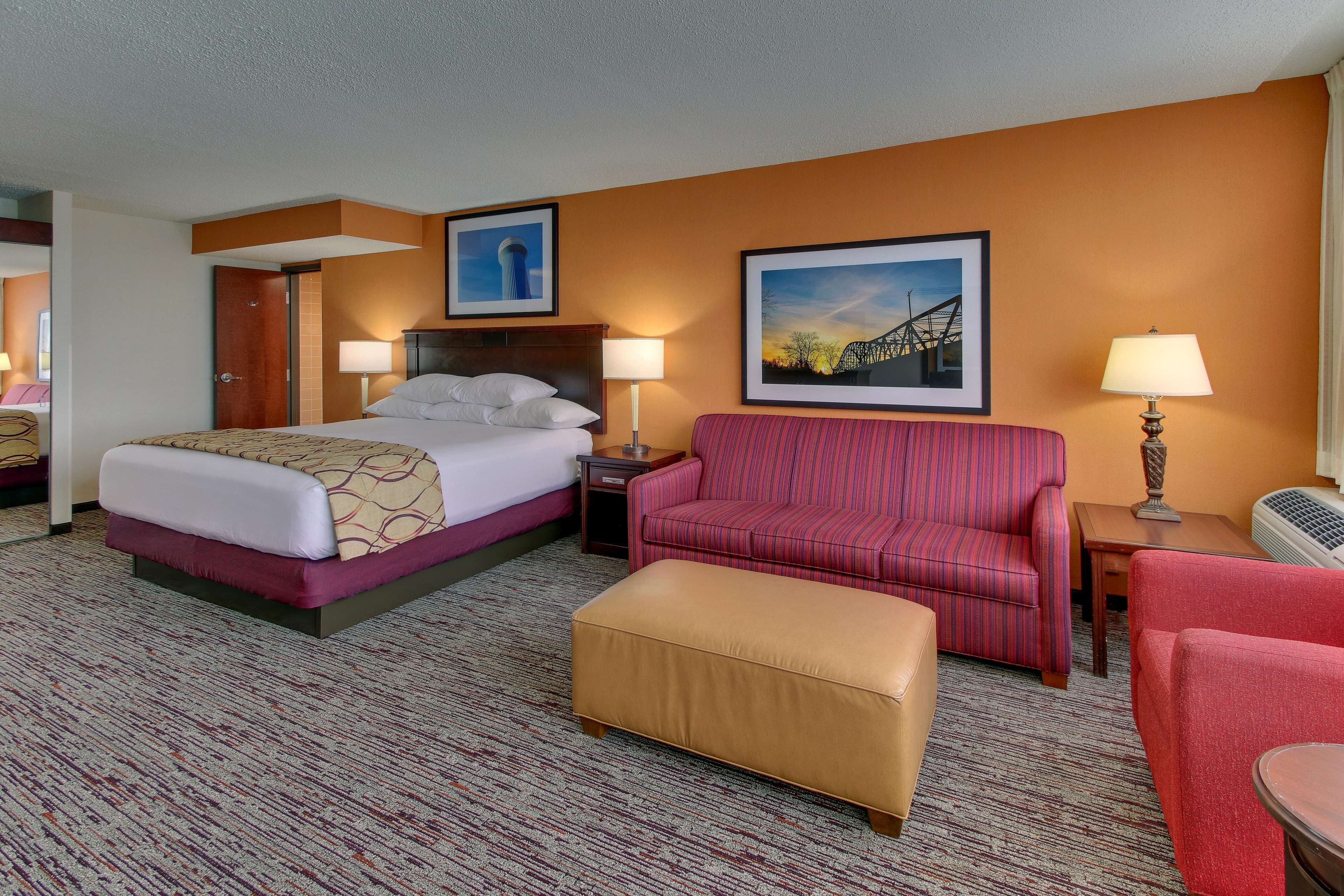 A hotel room with a bed, a red striped sofa, a small table, and a lamp.