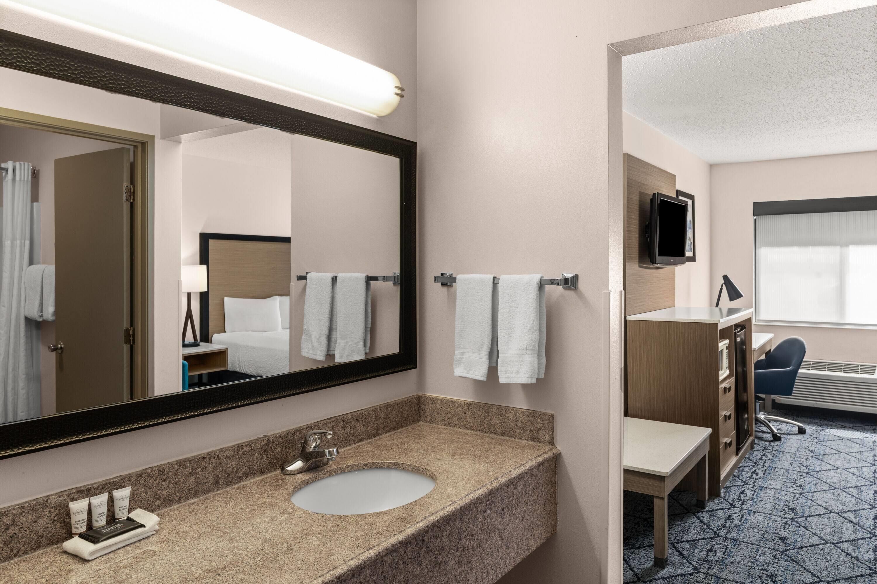 A hotel bathroom with a granite sink, a large mirror, and a towel rack.