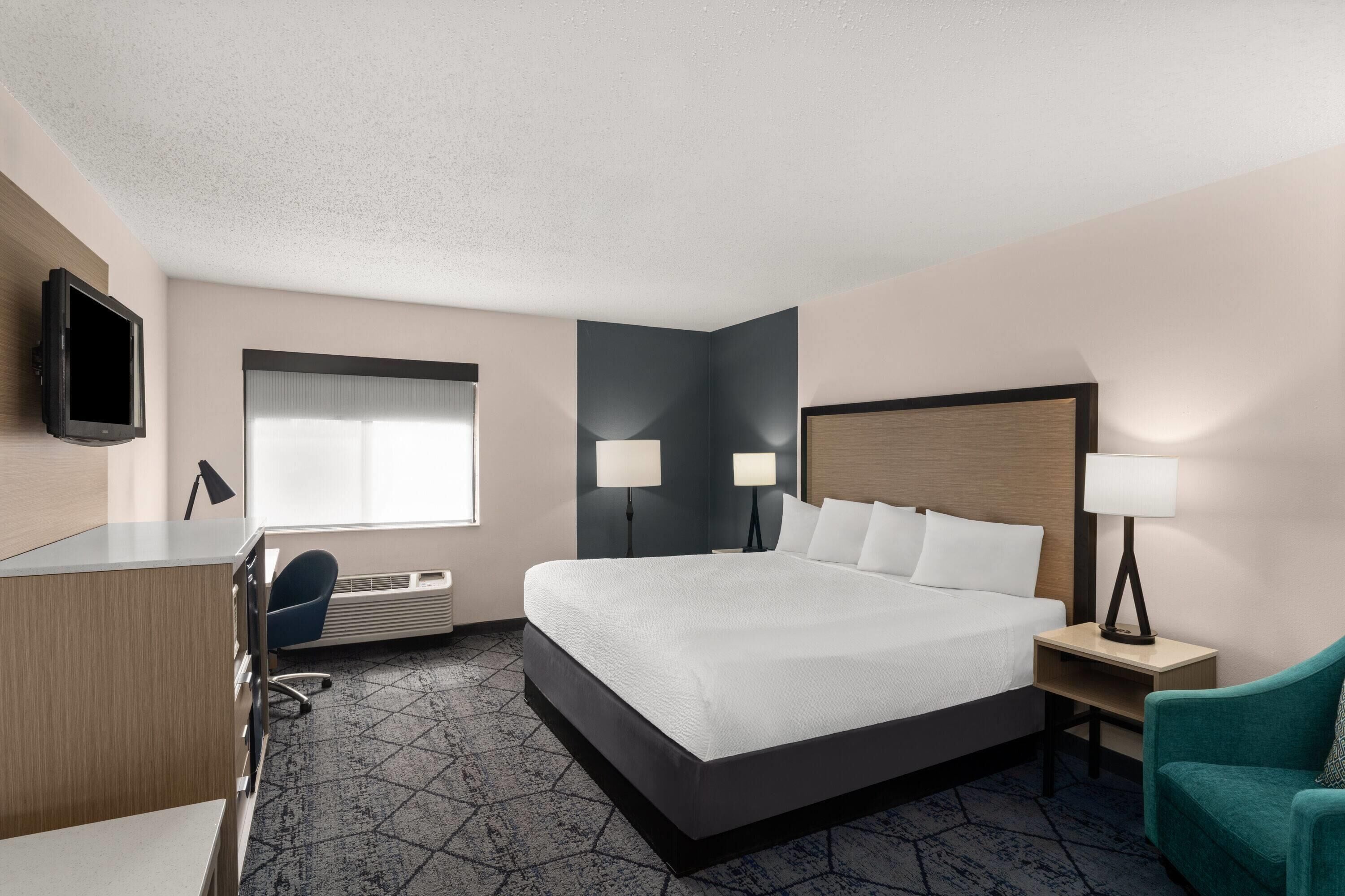 A hotel room with a bed, desk, chair, and two bedside lamps.