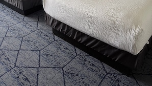 Une chambre d’hôtel avec deux lits, une table de chevet, une lampe et une moquette à motifs.