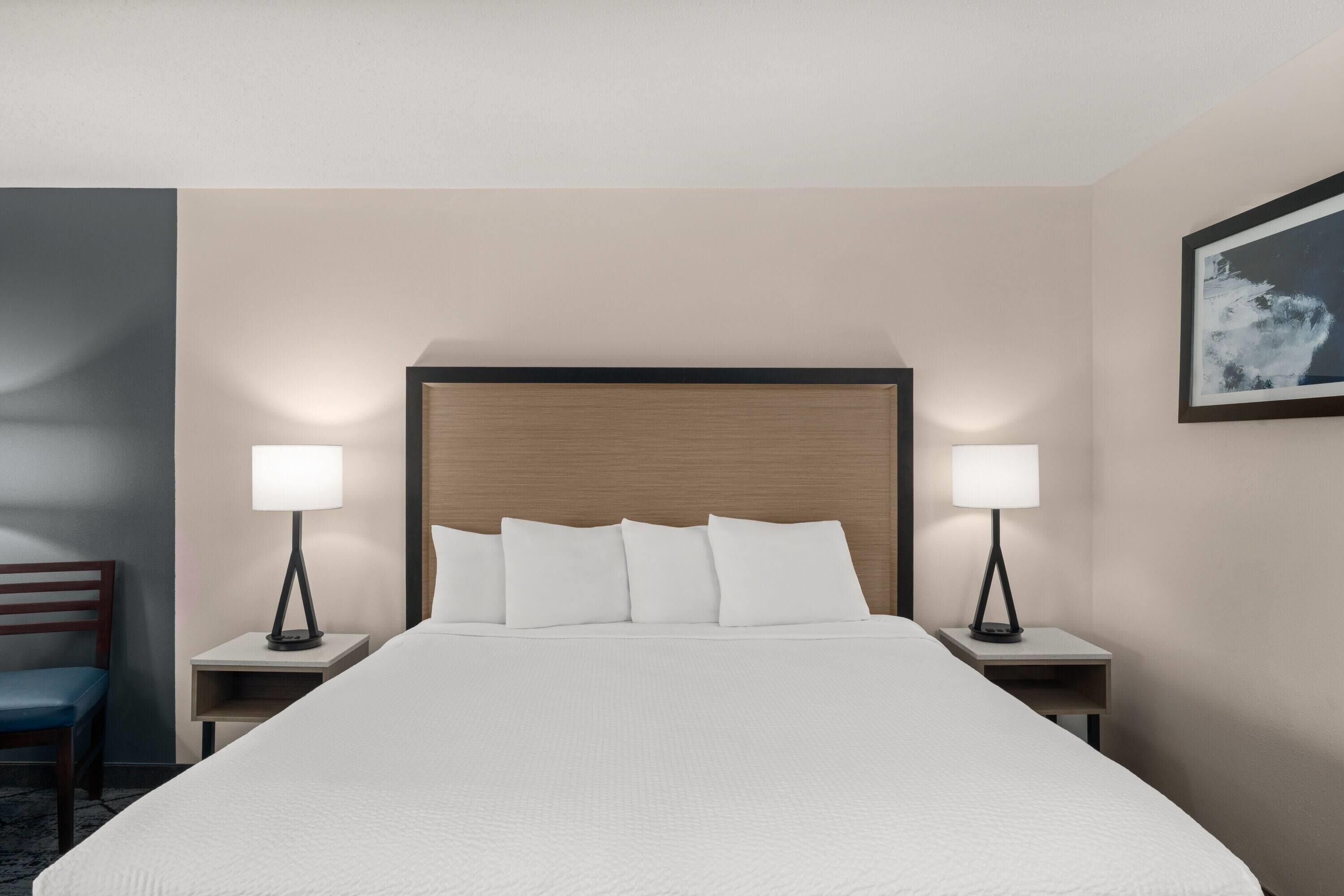 A hotel room with a large bed, two bedside tables, a chair, and a framed picture on the wall.