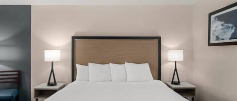 A hotel room with a large bed, two bedside tables, a chair, and a framed picture on the wall.