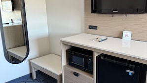 Une chambre d’hôtel compacte équipée d’un téléviseur à écran plat, d’un four à micro-ondes, d’un réfrigérateur, d’une banquette et d’une petite table.