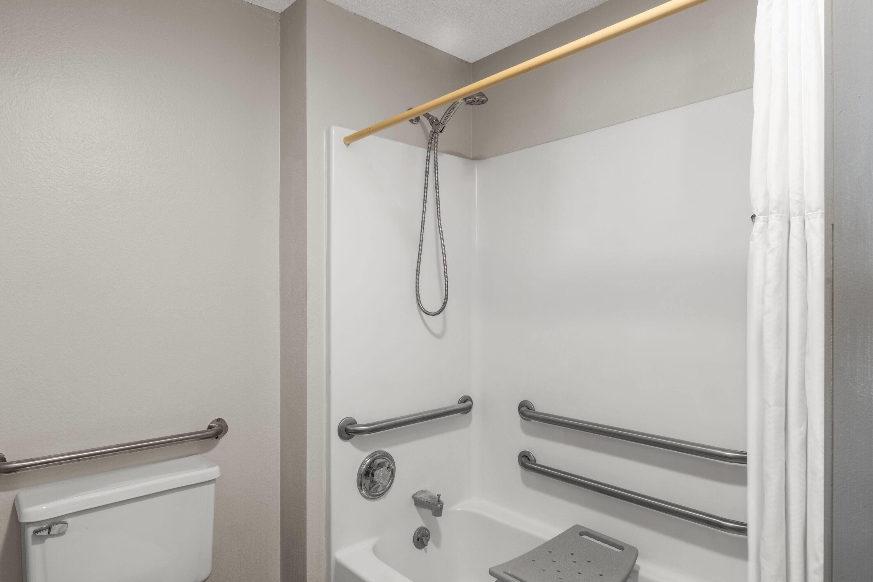 A bathroom with a shower, grab bars, and a toilet.