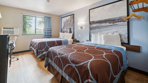 A hotel room with two beds, a desk, and a window with curtains.