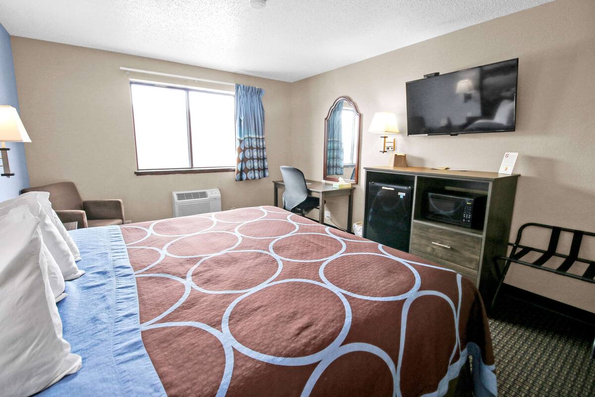 A hotel room with a large bed, a desk with a chair, a television, and a microwave.