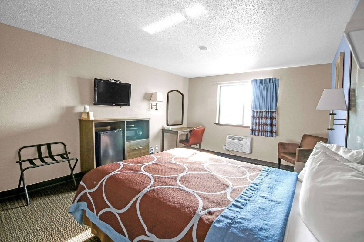 A hotel room with a bed, a desk, a chair, a television, and a window with curtains.
