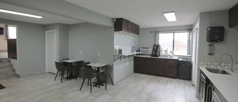 A modern kitchen with a dining area, featuring a central island, dark cabinets, and a large window.