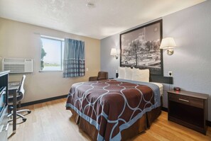 A hotel room with a large bed, a desk, an air conditioning unit, a nightstand, and a wall-mounted lamp. - Super 8 by Wyndham Kenosha/Pleasant Prairie (Pleasant Prairie)