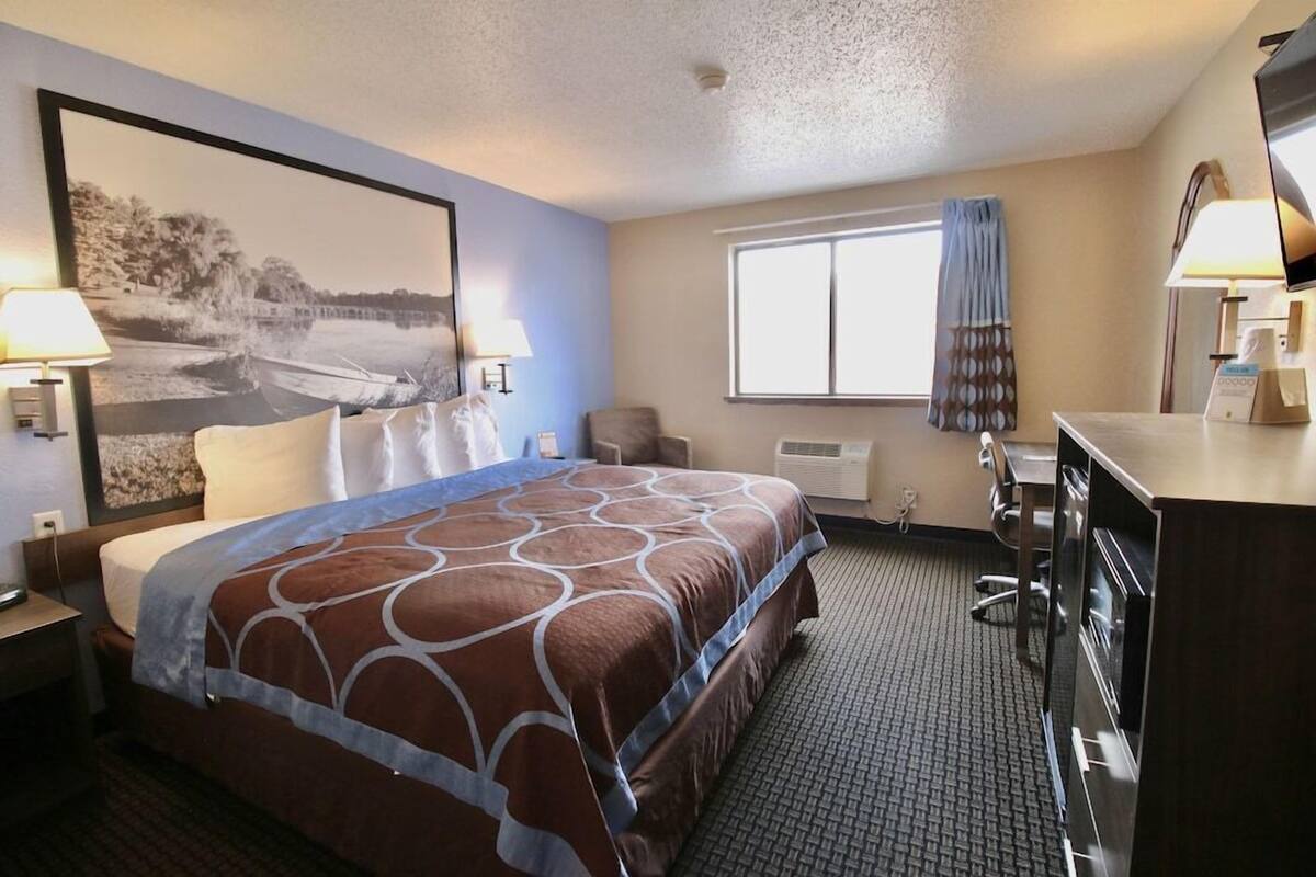 A hotel room with a bed, a desk, a chair, a television, and a window with curtains.