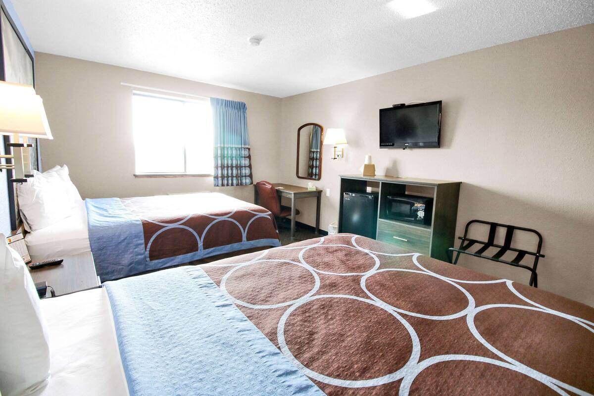 A hotel room with two beds, a desk, a chair, a TV, and a window with curtains.