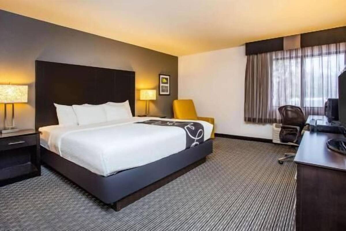A hotel room with a large bed, a desk, a chair, a TV, and a window with curtains.
