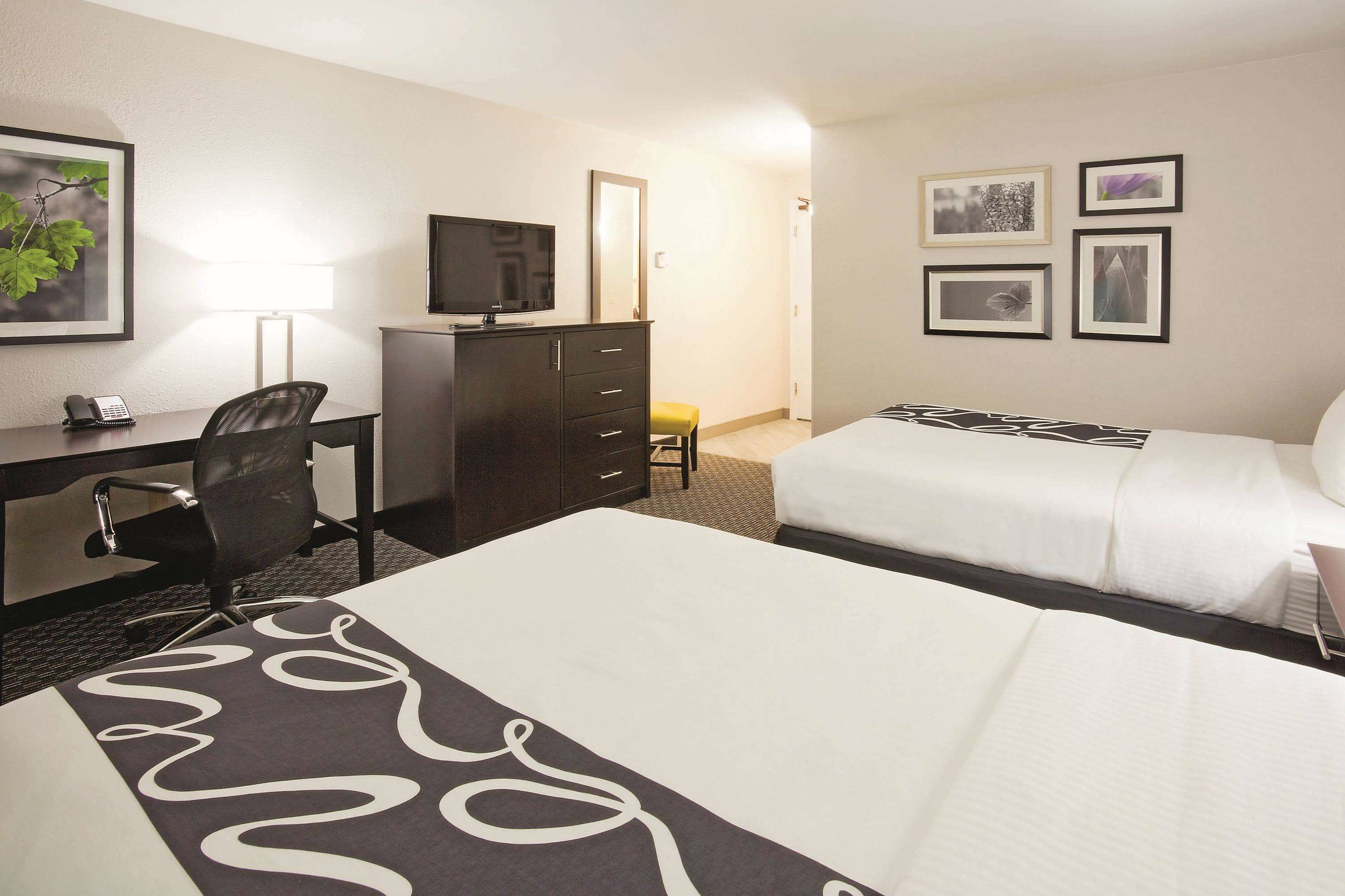 Una habitación de hotel con una cama, un escritorio con una silla, un televisor y un aparador.