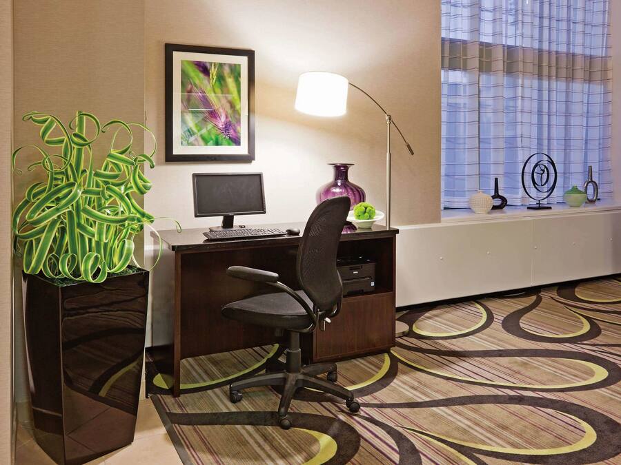 A hotel office with a desk, chair, computer, lamp, and decorative items.