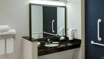 Un baño moderno con un lavamanos negro, encimera blanca y un espejo grande. Hay pasamanos blancos en las paredes y un perchero con toallas.