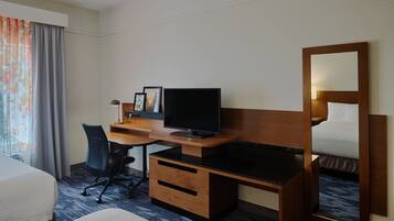 A hotel room with a bed, a desk with a computer, a chair, and a large mirror.