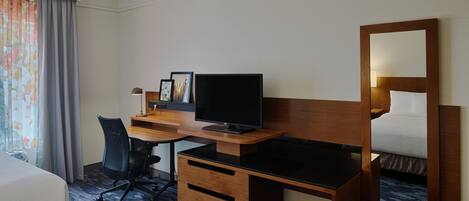 A hotel room with a bed, a desk with a computer, a chair, and a large mirror.