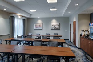 A conference room with a long table, multiple chairs, framed artwork on the walls, and a coffee machine in the corner.