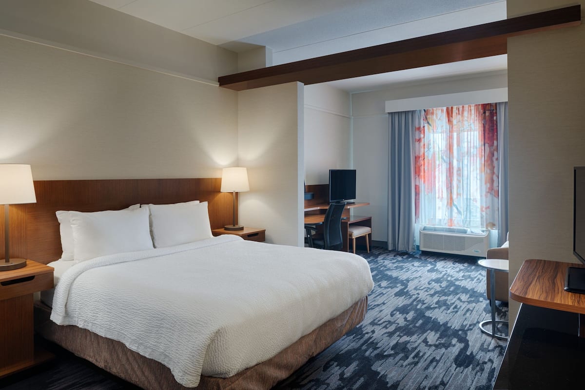 A hotel room with a large bed, two bedside tables with lamps, a desk with a chair, a television, and a window with curtains.