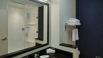 A modern bathroom with a large mirror, a black countertop, a white sink, and a towel rack with folded towels.