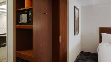 A hotel room with a wooden wardrobe, a microwave, and a bed with a white pillow.