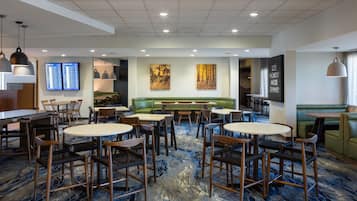 A hotel lobby with a seating area, tables, and a digital display board.