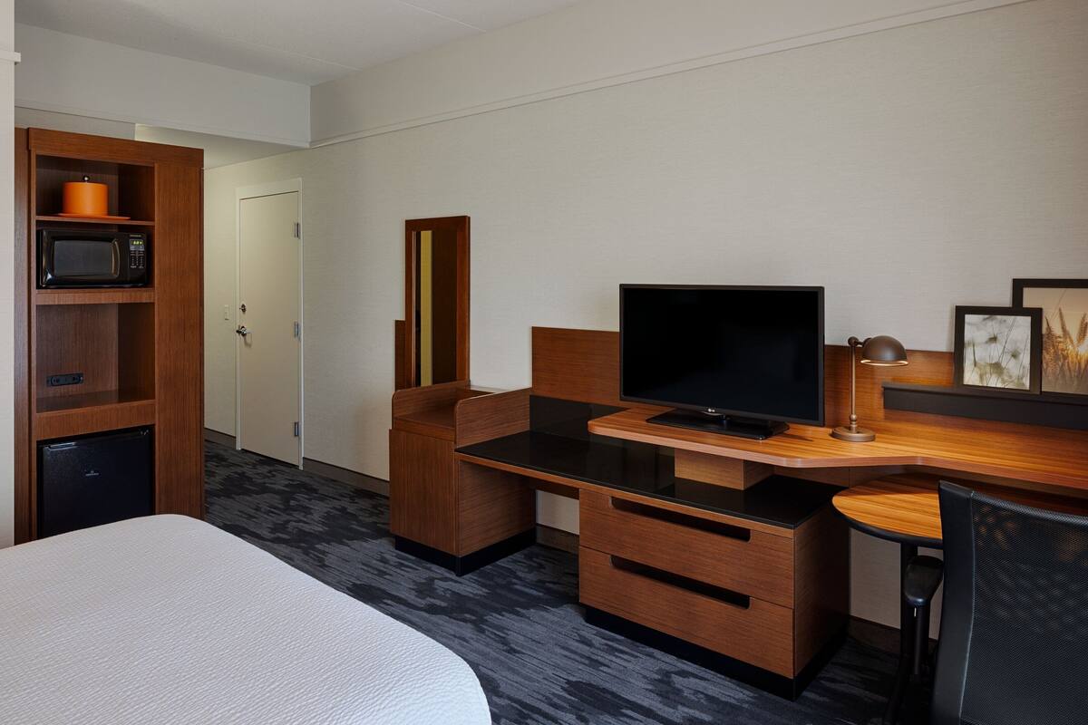 A hotel room with a bed, a desk with a TV, a microwave, and a small fridge.