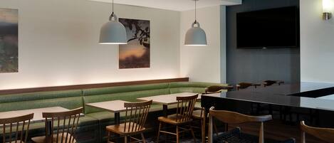 Un restaurant avec des banquettes, des tables et des chaises, un téléviseur à écran plat et des luminaires suspendus.