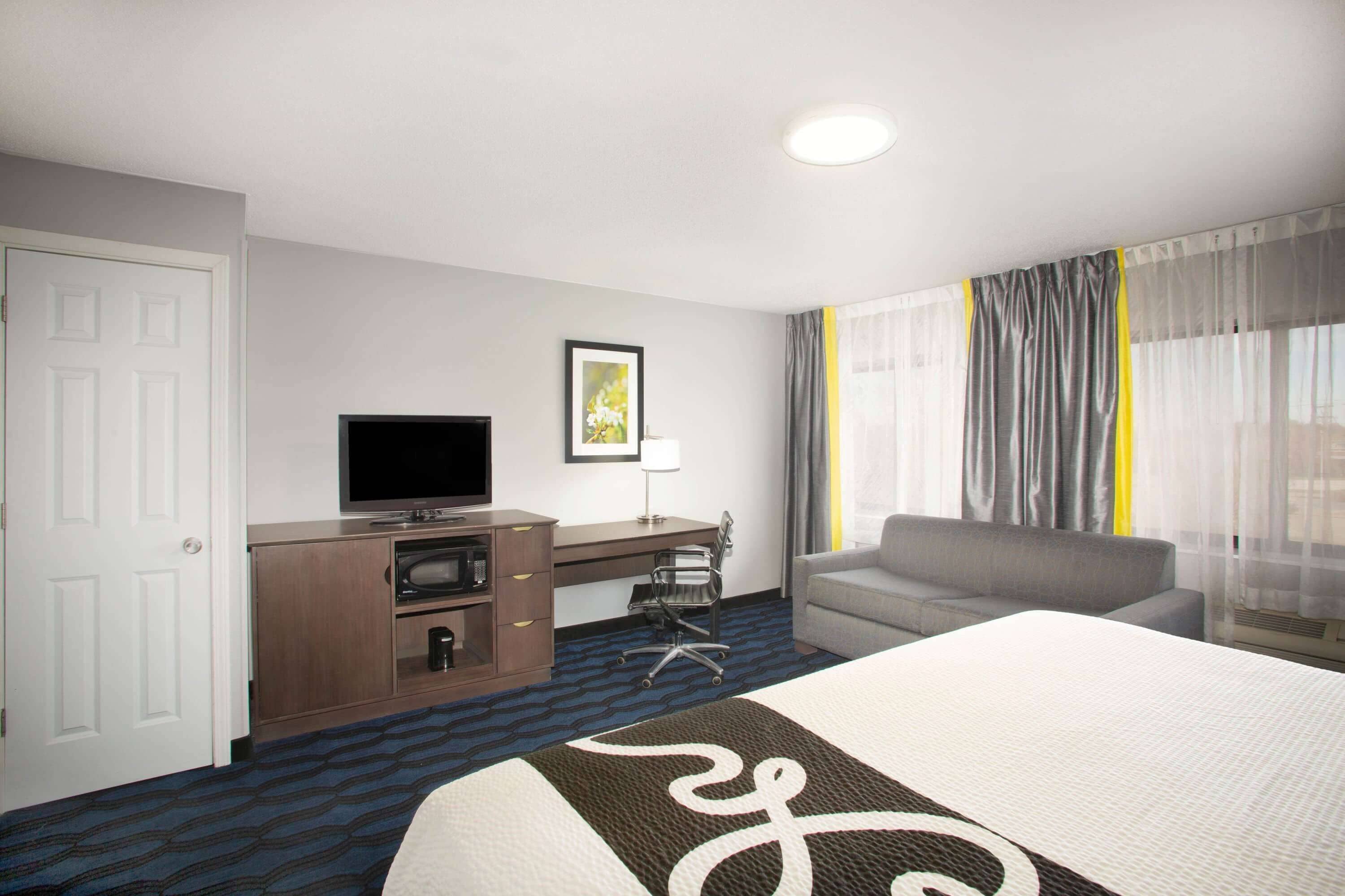 A hotel room with a bed, a desk with a television, a chair, and a window with curtains.