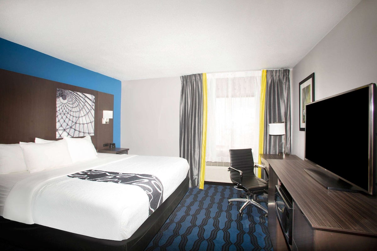 A hotel room with a large bed, a desk with a flat-screen TV, and a chair.