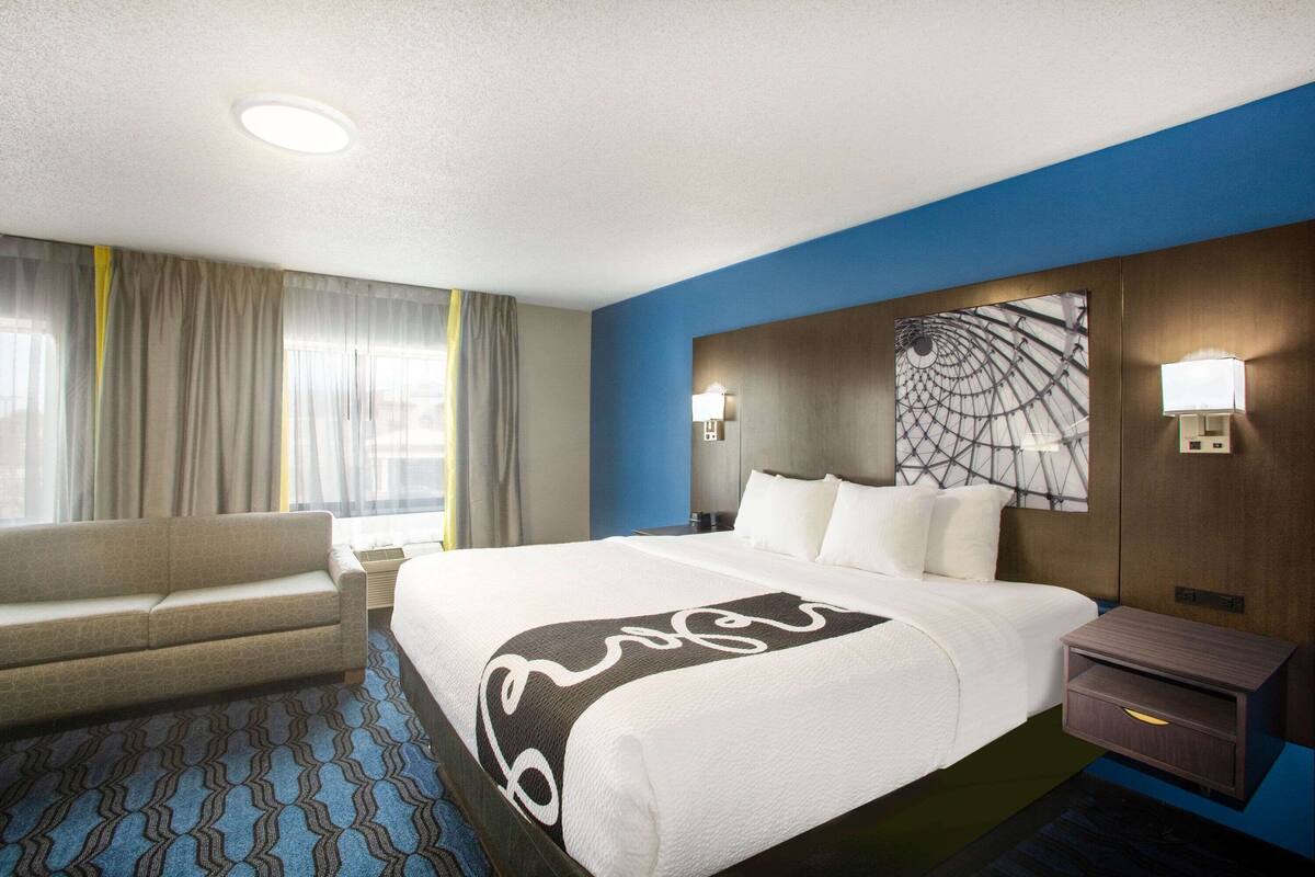 A hotel room with a large bed, a sofa, a desk, and a window with curtains.