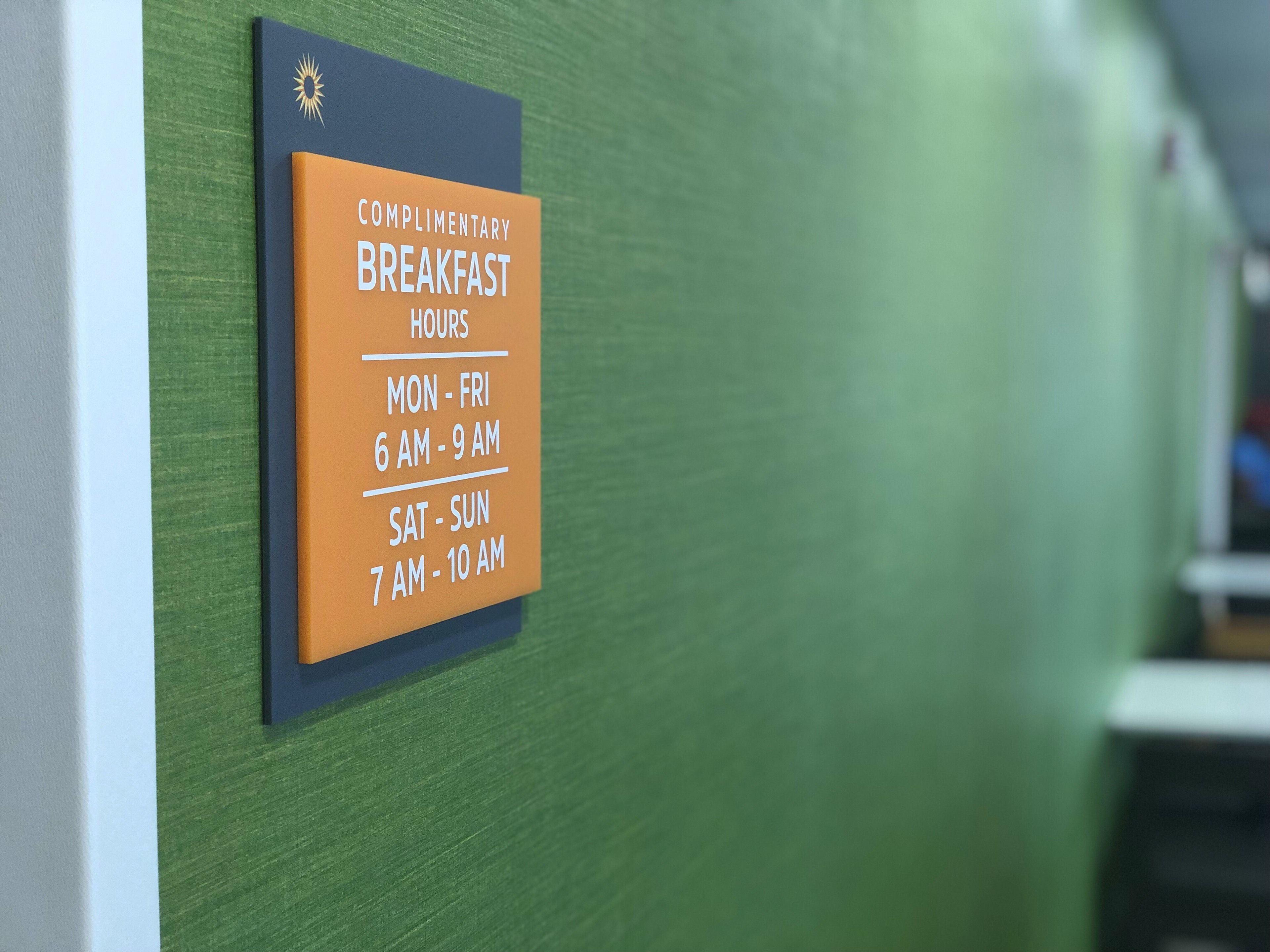 A sign indicating complimentary breakfast hours: Mon-Fri 6 AM-9 AM, Sat-Sun 7 AM-10 AM.