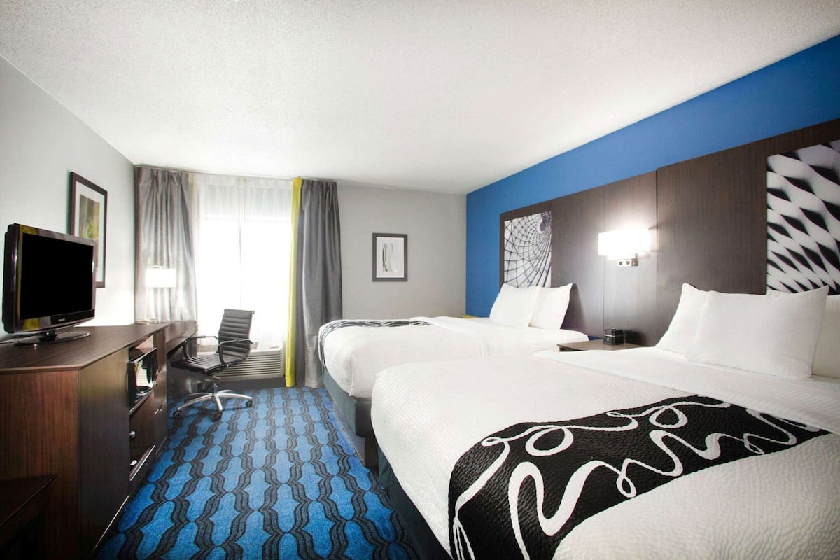 A hotel room with two beds, a desk with a TV, a chair, and a patterned carpet.
