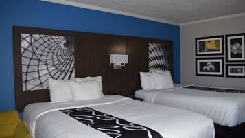 Habitación de hotel con dos camas, cabecera de diseño geométrico, lámpara de pared e imágenes enmarcadas.