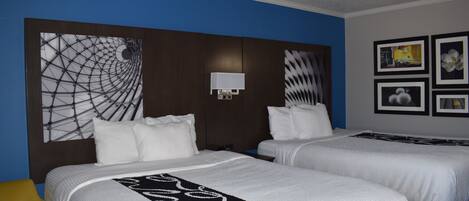 Een hotelkamer met twee bedden, een hoofdbord met een geometrisch patroon, een wandlamp en ingekaderde foto's.