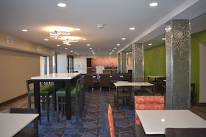 Un hall d’hôtel moderne doté de plusieurs espaces de détente, comprenant des tables et des chaises, ainsi qu’un tapis à motifs.