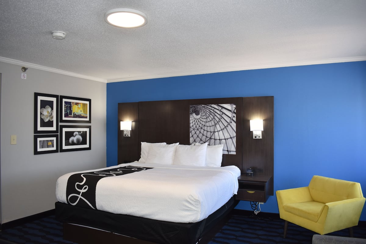 A hotel room with a large bed, a yellow armchair, and artwork on the walls.