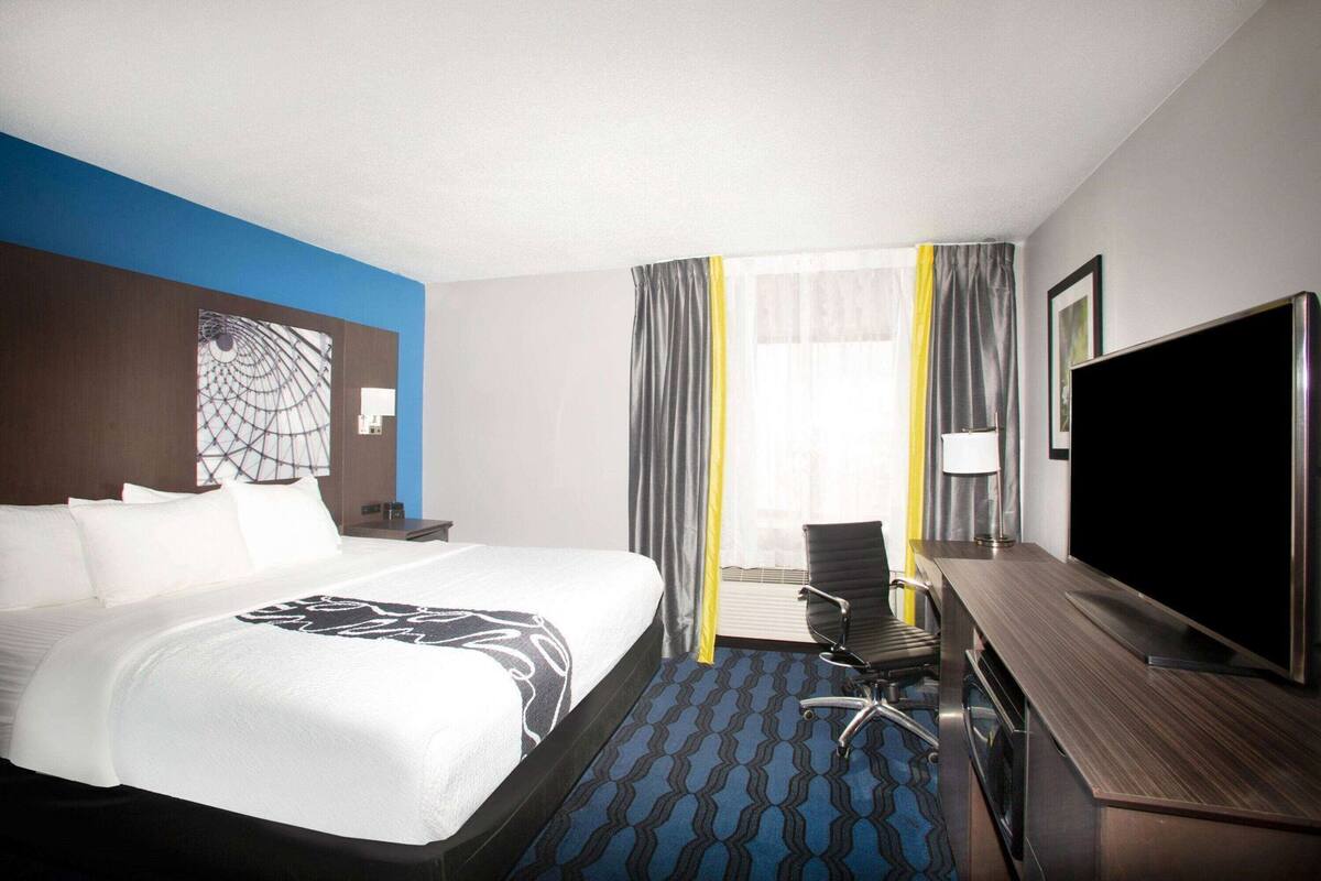 A hotel room with a bed, a desk, a chair, a TV, and a window with curtains.