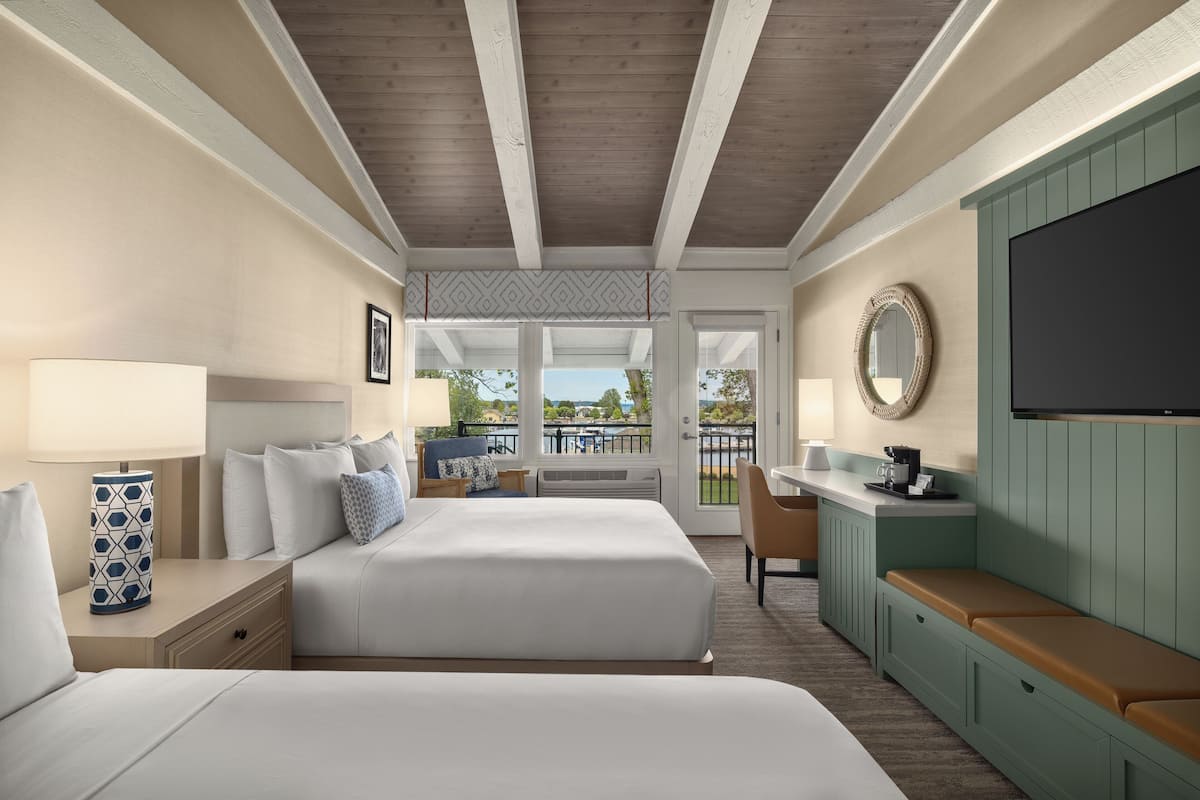 A hotel room with two beds, a desk, a TV, and a balcony with a view.