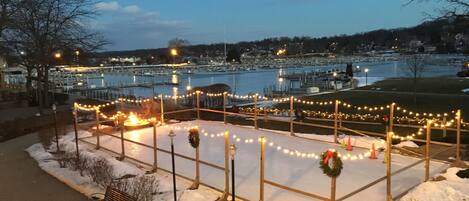A snow-covered outdoor area with benches and string lights, overlooking a marina and water.