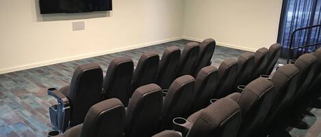 Un cine con filas de asientos, una pantalla grande y piso alfombrado.