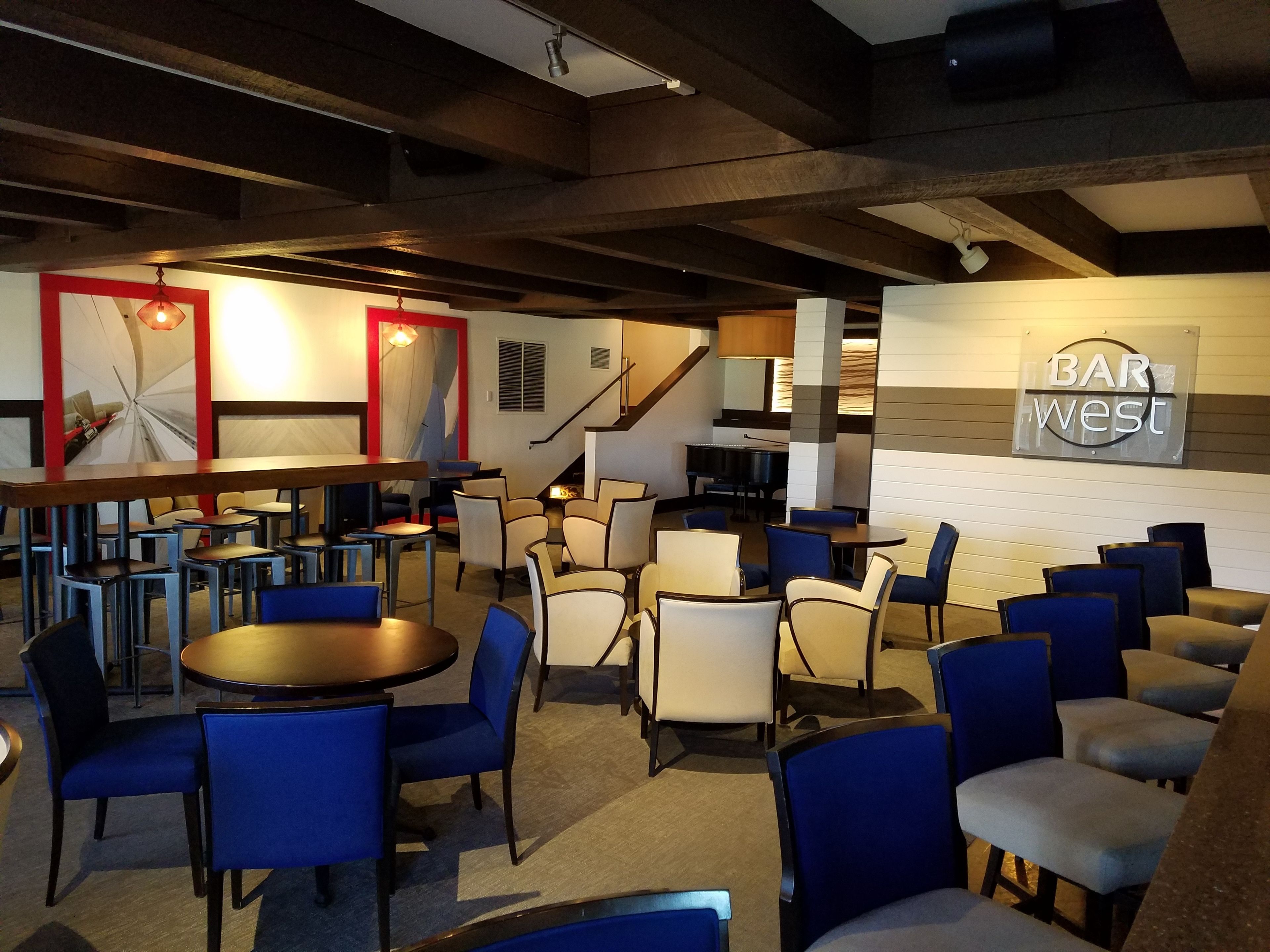 A bar area with multiple seating arrangements, a piano, and a staircase leading to an upper level.