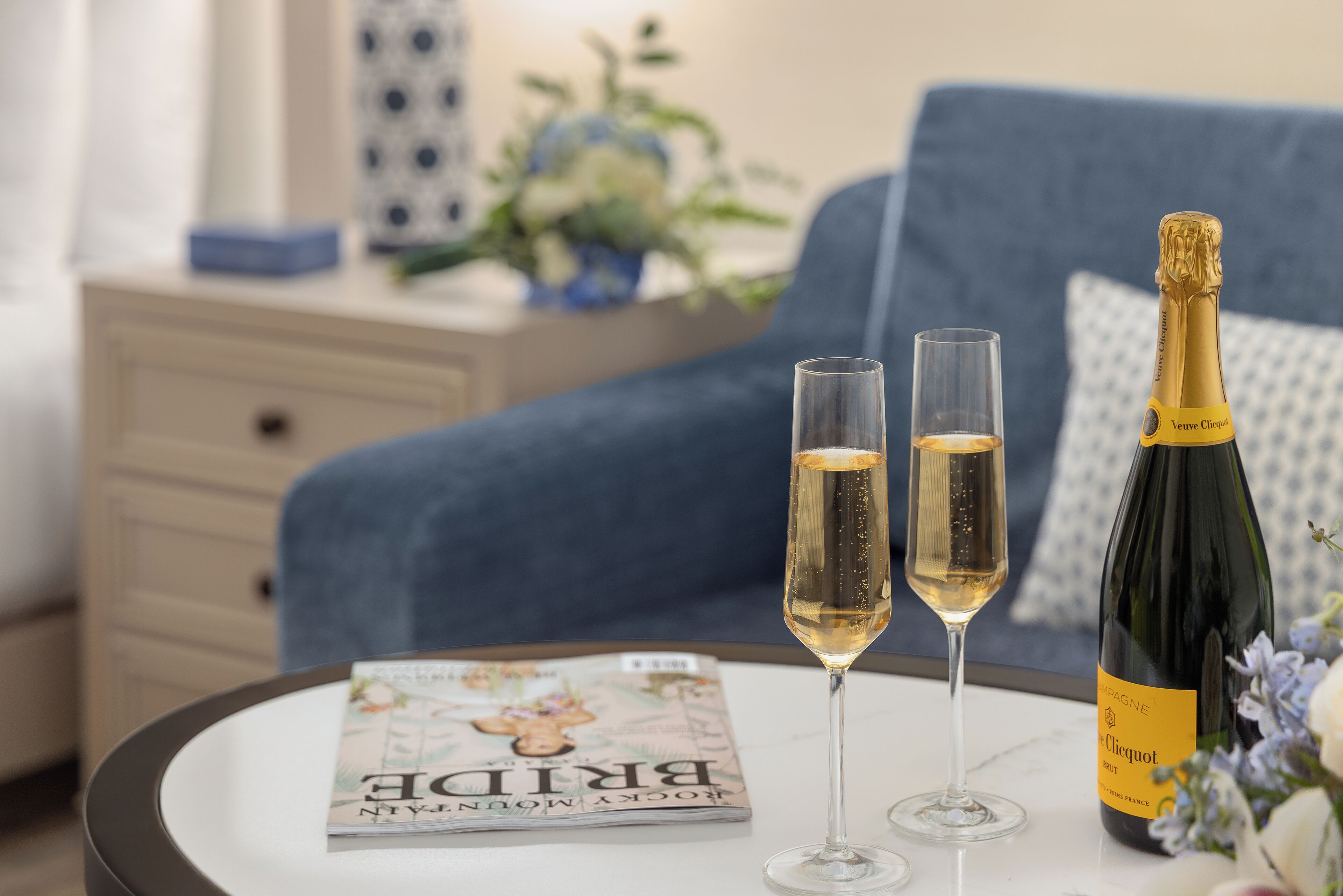 A magazine on a table, two glasses of champagne, and a bottle of wine.
