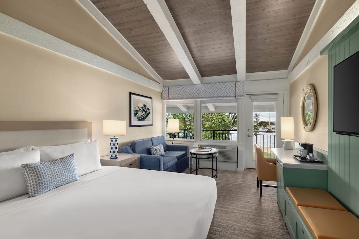 A hotel room with a large bed, a sofa, a small table, and a kitchenette area.