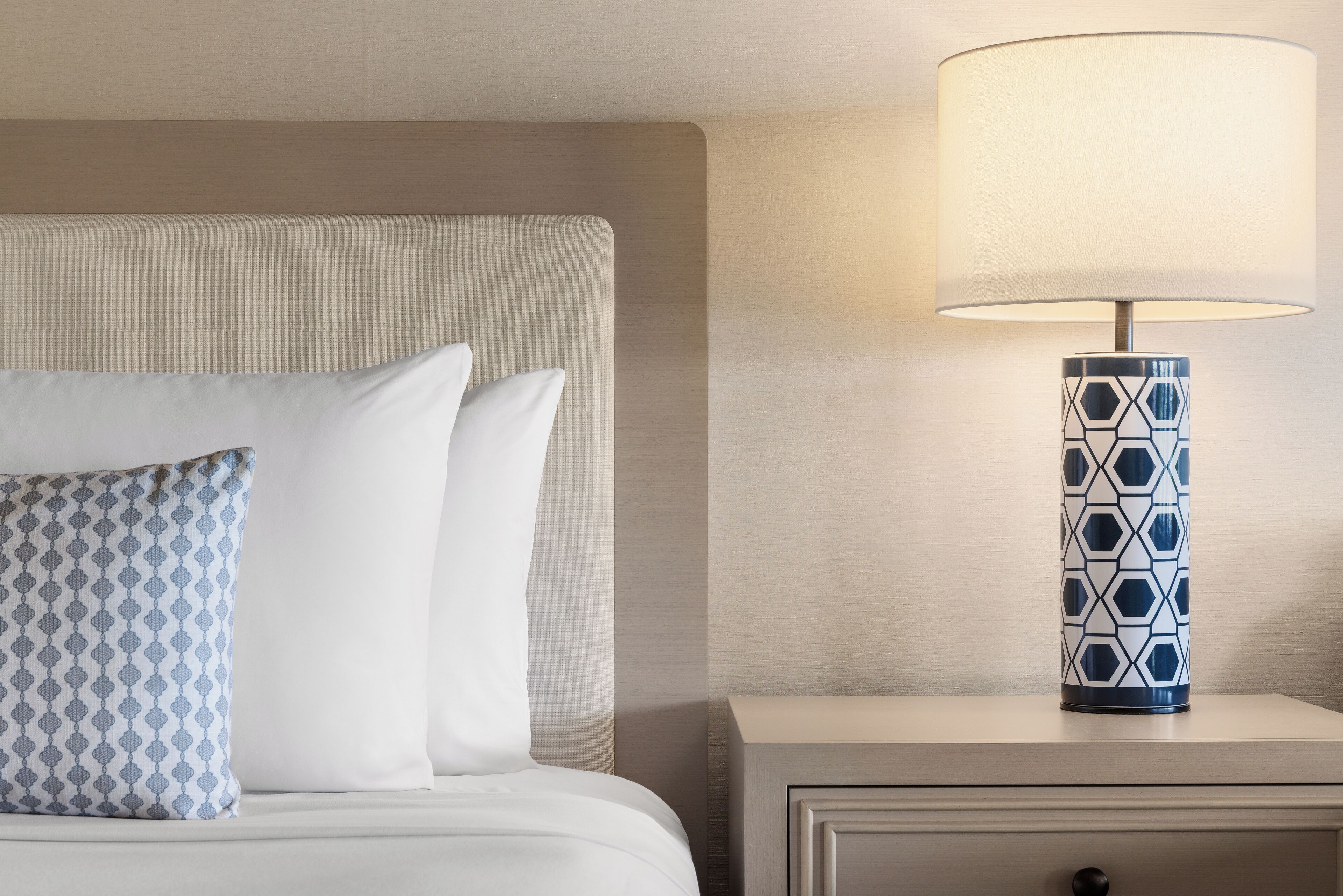 A neatly made bed with patterned pillows, a bedside lamp, and a nightstand with a drawer.