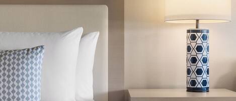 A neatly made bed with patterned pillows, a bedside lamp, and a nightstand with a drawer.
