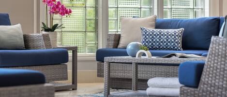 A modern living room with a blue sofa, wicker furniture, and a large window with a view.