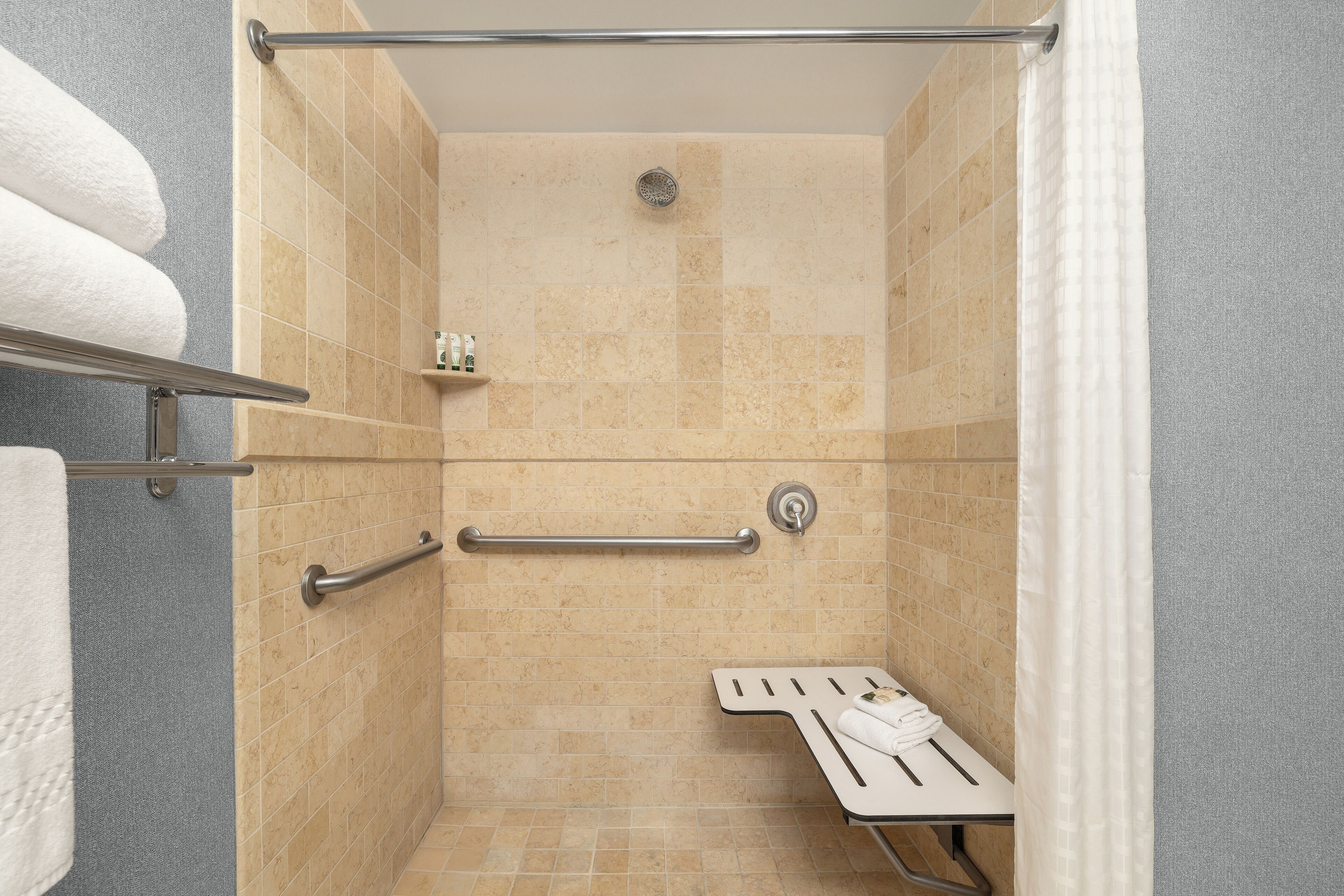 A shower with beige tiles, a grab bar, a towel rack, and a showerhead.