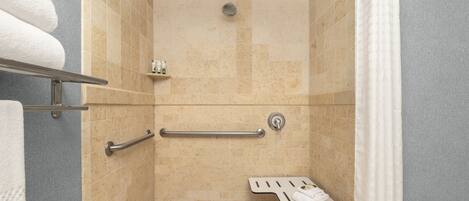 A shower with beige tiles, a grab bar, a towel rack, and a showerhead.