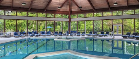 Una amplia piscina interior con varias pistas de natación, rodeada de sillones de descanso y una cubierta.